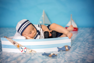 Sticker - Cute toddler baby boy sleeping in wooden boat with fishes, starfish and binoculars, dressed as sailman