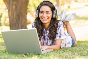 Poster - Pretty brunette lying in the grass and using laptop