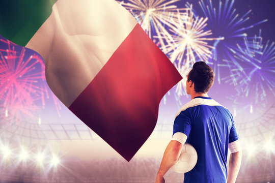 Handsome italian football player in blue jersey against fireworks exploding over football stadium