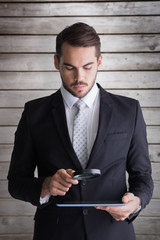 Canvas Print - Concentrated businessman using magnifying glass against wooden planks