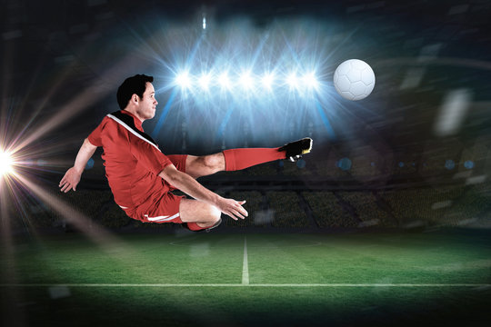 Football player in red kicking in a football pitch under spotlights