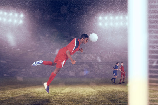Football player in red jumping against large football stadium under blue sky