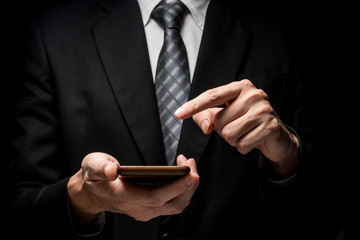 Wall Mural - Close up of man in black suit using smart phone on black background