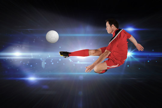 Football player in red kicking against black background with spark