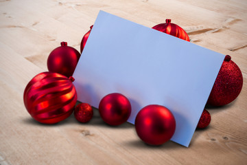 Leinwandbilder - Red christmas baubles surrounding white page against bleached wooden planks background
