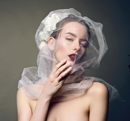 Beautiful young girl close-up in the image of the bride. A white veil on his face, flowers in his hair.