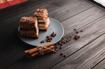 Wall Mural - Sweet dessert tiramisu in a cut on a gray plate on a black wooden background with spices: cinnamon sticks and badan, coffee beans