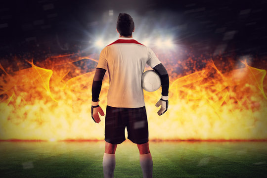 Goalkeeper standing in white jersey against football pitch under spotlights