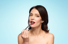 beauty, cosmetics and people concept - beautiful young woman with make up brush applying red lipstick over blue background