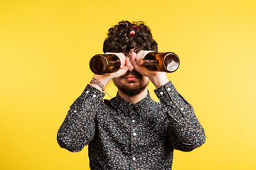 Wall Mural - Studio portrait of a young man holding bottles on a yellow background.