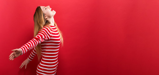 Wall Mural - Happy young woman with her arms outstretched on a red background