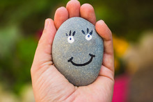 Hand Holding A Rock With A Happy Face Painted On It