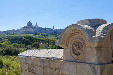 Old burial crypt cemetery below the Ancient hilltop fortified capital city of Malta, The Silent City, Mdina or L-Imdina, it's skyline against blue skies with huge walls, domes and towers, March 2017