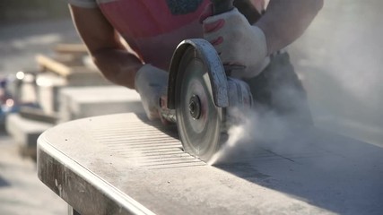 Wall Mural - Worker in gloves with a big angle grinder cuts a granite slab. Stone processing from rock.