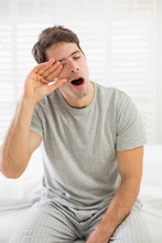 Sleepy Man Yawning As He Rubs His Eye In Bed