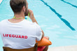 Lifeguard sitting on chair and blowing whistle at poolside