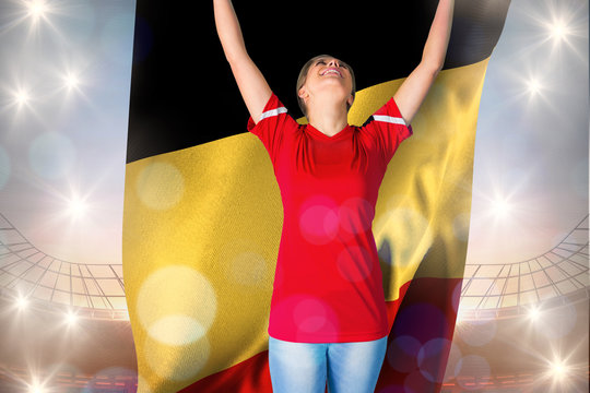 Cheering football fan in red holding belgium flag against large football stadium under blue sky