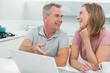 © WavebreakmediaMicro - Cheerful couple in conversation while using laptop in kitchen