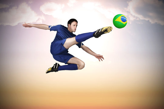 Football player in blue kicking against beautiful orange and blue sky