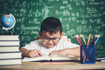 Wall Mural - boy reading a book sitting at the table in the classroom