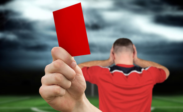 Composite image of hand holding up red card to player against football pitch under stormy sky