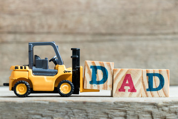 Wall Mural - Toy yellow forklift hold letter block D to complete word dad on wood background (Concept of father day)