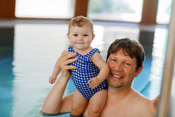 Wall Mural - Happy middle-aged father swimming with cute adorable baby girl in swimming pool.