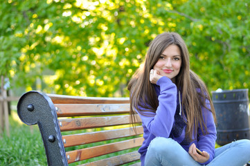 portrait of a young beautiful woman in a purple sports blazer that sits on a bench in the park and s