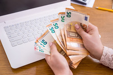 Hands Of Businesswoman Counting Euro Banknotes On Laptop Keyboard