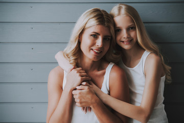 Wall Mural - Blonde cute girl hugs blonde mother on wooden background.