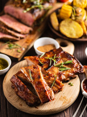 Wall Mural - Delicious barbecued ribs seasoned with a spicy basting sauce and served with chopped fresh vegetables on an old rustic wooden chopping board