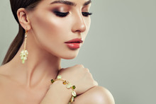 Closeup Portrait Of Young Woman With Jewelry. Female Face With Makeup, Gold Bracelet And Earrings With Green Gem