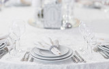Fototapeta  - Silver cutlery and stylish white plates are laid out on a white tablecloth of expensive fabric in a restaurant for a festive banquet