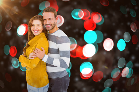 Portrait of happy young couple embracing against digitally generated twinkling light design 