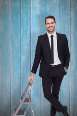 Poster - Smiling businessman leaning on stepladder against wooden planks