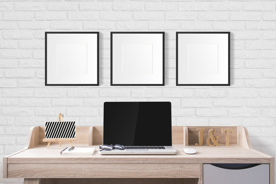 notebook computer and stationery on working table with blank photo frames in the studio with white brick wall.
