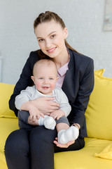 Wall Mural - beautiful smiling businesswoman sitting on sofa with little son