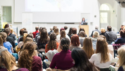 female speaker giving presentation in lecture hall at university workshop. audience in conference ha