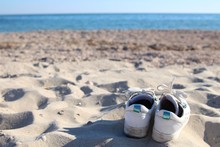 A Pair Of White Sneakers With Shoelaces Abandoned On The Beach