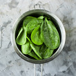 Washed spinach in a metal colander on a gray background. Fresh green leaves for cooking healthy dishes