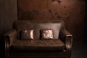 Brown leather sofa in the dark loft room with small shiny pillows