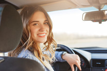 Close Up Portrait Of Pleasant Looking Female With Glad Positive Expression, Being Satisfied With Unforgettable Journey By Car, Sits On Driver`s Seat, Enjoys Music. People, Driving, Transport Concept