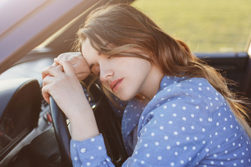 Wall Mural - Exhausted overworked female driver can`t drive car any more, naps on wheel, feels sleepy and tired, has headache. Fatigue woman feels tired after driving in rush hour. Tiredness and driving concept