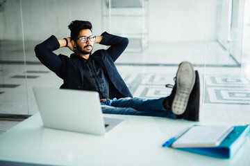 Young indian Businessman working in his office with feet on desk