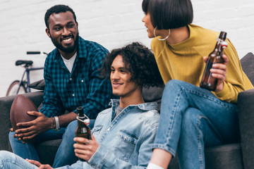 Wall Mural - young multicultural friends with bottles of beer and ball for american football