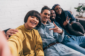 Wall Mural - young mixed race woman taking selfie with multiethnic friends doing peace gesture