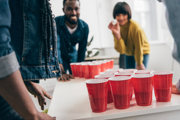 Wall Mural - cropped shot of multicultural group of friends playing beer pong at table