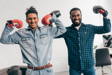 Wall Mural - two smiling young men in boxing gloves standing with arms raised