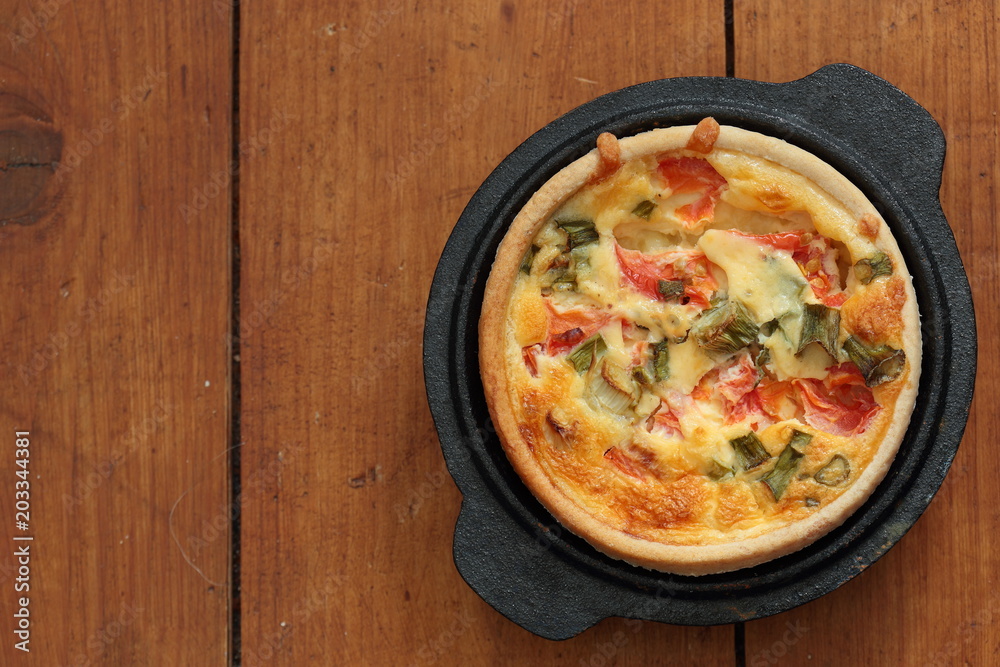 Tomato and spring onion quiche in a cast iron pot dish on a wood ...