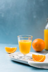 Glass of fresh orange juice with orange slices on white plate, blue background, cold summer refreshing nutritional beverage, blue orange color contrast, vitamin C healthy drink, copy space